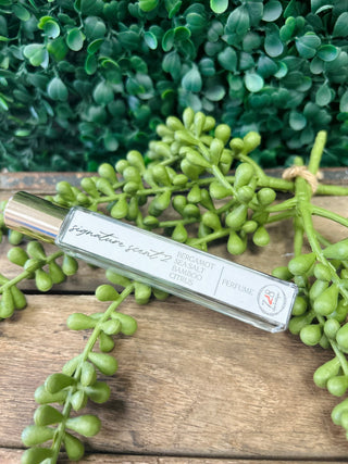 Vincent 728 Signature Perfume bottle with silver cap on wooden surface surrounded by green succulent plants.