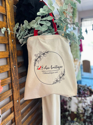 Cream canvas tote bag with 728 chic boutique logo and floral design hanging with eucalyptus branches