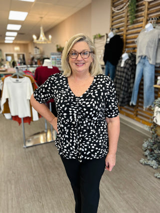 Woman wearing black and white polka dot ruched top in clothing store setting