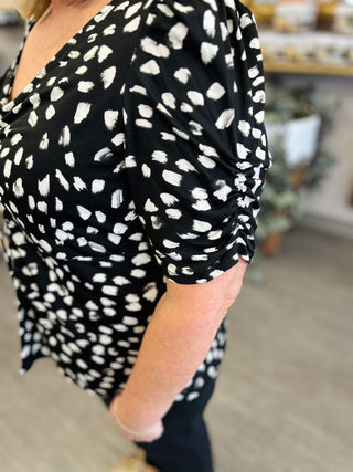 Woman wearing black and white abstract print ruched top with gathered sleeves in retail setting