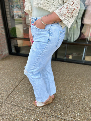 Woman wearing light blue distressed cropped straight leg jeans with white lace top and sandals