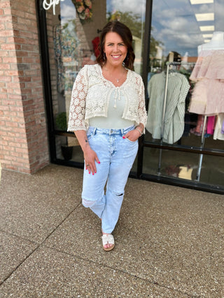 Woman wearing light blue distressed cropped jeans with white lace top standing outside clothing store