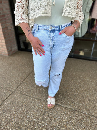 Woman wearing light blue distressed cropped jeans with white lace top and pink sandals.