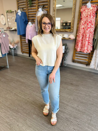 Woman wearing cream sleeveless knit sweater vest with jeans in clothing boutique store