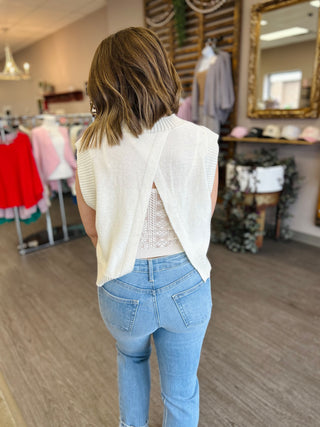 Woman wearing cream knit sleeveless top with open back detail and jeans in clothing boutique