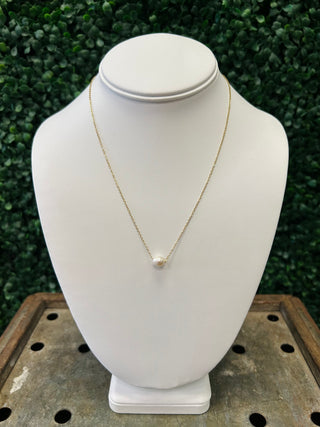 Delicate gold chain necklace with single pearl pendant displayed on white jewelry bust stand.