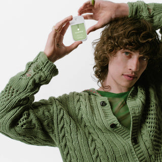 Person in green knit sweater holding Touchland hand sanitizer spray bottle in cupped hands
