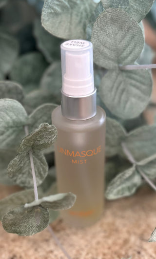 Clear glass spray bottle with pink pump surrounded by green eucalyptus leaves on wooden surface.