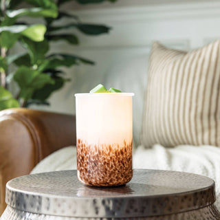 Ambre Illumination Fragrance Warmer glowing on wooden table in cozy living room setting with plants