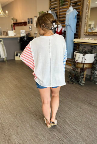 Woman wearing striped sleeve top and denim shorts in boutique store, viewed from behind.