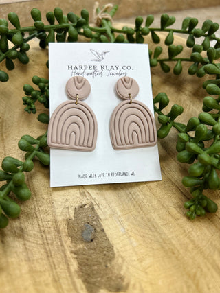 Harper Klay Co handcrafted clay earrings with rainbow arch design displayed on card with green plants