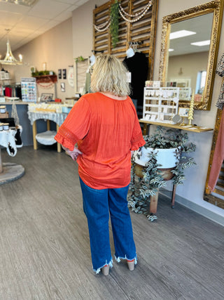 Woman wearing red eyelet top with ruffled sleeves and jeans, standing in boutique interior with mirrors.