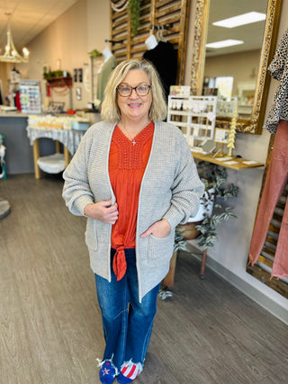 Woman wearing red eyelet top with gray cardigan and jeans in retail store setting