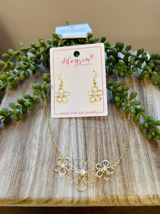 Gold flower-shaped earrings and matching necklace set displayed on jewelry card with green succulent plants.