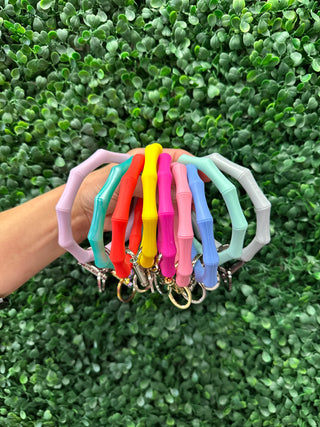 Hand holding colorful bamboo-style keyrings with metal clasps against green foliage background