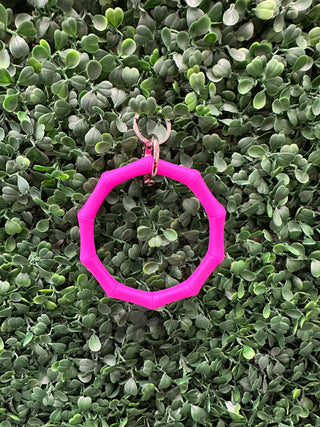 Pink octagonal bamboo keyring with metal clasp displayed on green succulent plant background