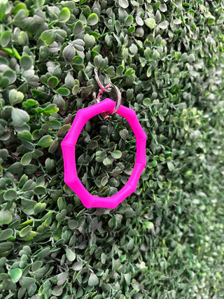 Pink octagonal bamboo keyring hanging on green succulent plant foliage background.
