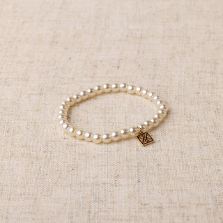 Michelle McDowell Basic Pearl Stretch Bracelet with gold brand charm tag on linen background.