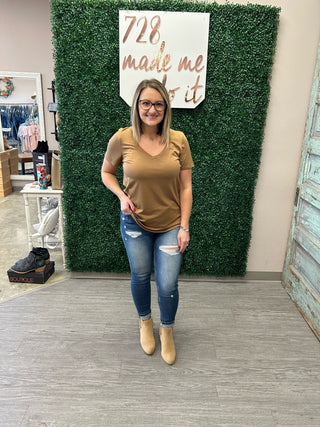Woman wearing mustard yellow basic v-neck tee with distressed jeans and tan boots in boutique setting.