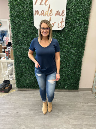 Woman modeling navy blue v-neck tee with distressed jeans and tan boots in boutique setting