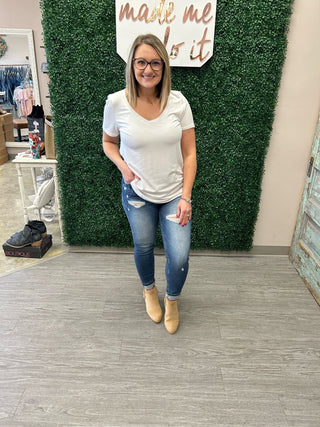 Woman wearing white basic v-neck tee with distressed jeans and tan boots in boutique setting