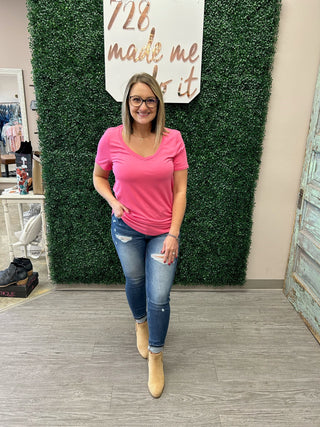 Woman wearing pink v-neck tee with distressed jeans and tan boots in boutique setting