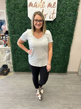 Woman modeling white v-neck tee with black leggings and patterned boots in boutique setting.