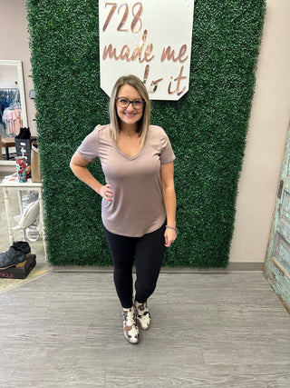 Woman wearing basic v-neck tee and black pants, standing in boutique with green wall backdrop.