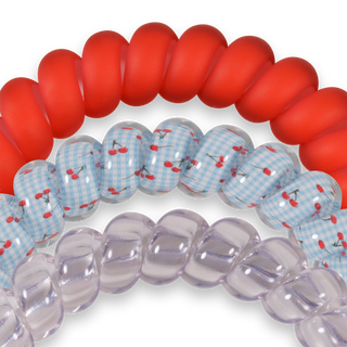 Three colorful hair ties with red, blue gingham cherry print, and clear purple designs on black background.