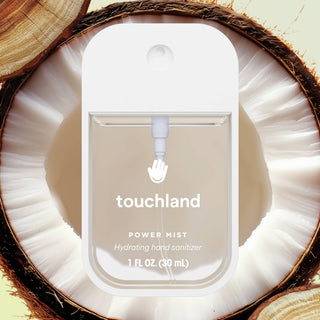 Touchland Power Mist hydrating hand sanitizer bottle displayed inside a halved coconut shell with tropical styling.