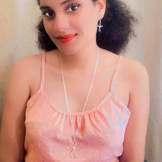 Young woman wearing Alegria Accessories Believe cross-shaped silver dangle earrings with matching necklace.