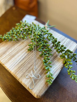 Silver wire initial "H" pendant necklace on delicate chain displayed on wooden board with greenery.