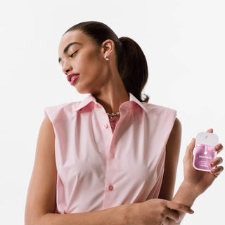 Woman in pink sleeveless shirt holding Touchland Berry Bliss Power Mist hand sanitizer bottle.