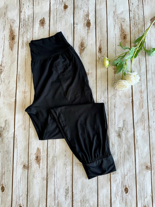 Black joggers with elastic waistband and cuffed ankles laid flat on rustic wooden background with flowers