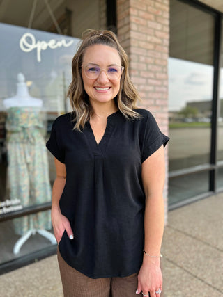 Woman smiling outside boutique wearing a short-sleeve V-neck blouse with cuffed sleeves.