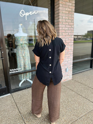 Woman wearing Blu Pepper button-back blouse with brown wide-leg pants outside boutique.