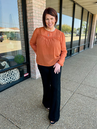 Woman wearing black high-rise flare jeans with orange polka dot top, standing outside storefront.