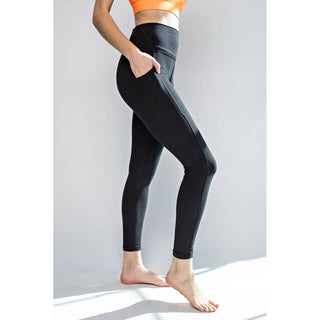 Woman wearing black high-waisted leggings with side pockets and orange sports bra, standing barefoot.