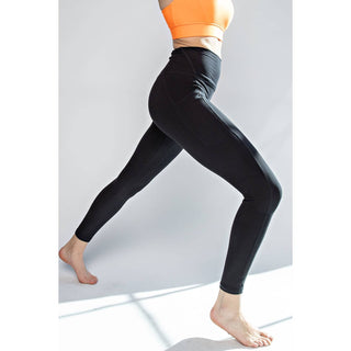 Woman wearing black high-waisted leggings and orange sports bra in dynamic pose against white background