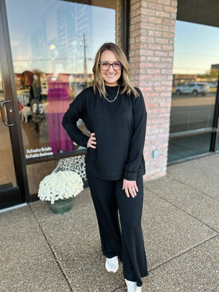 Woman wearing black ribbed mock neck sweater and matching wide-leg pants set, standing outdoors