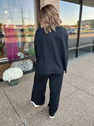 Woman wearing black ribbed mock neck sweater and matching pants set, viewed from behind