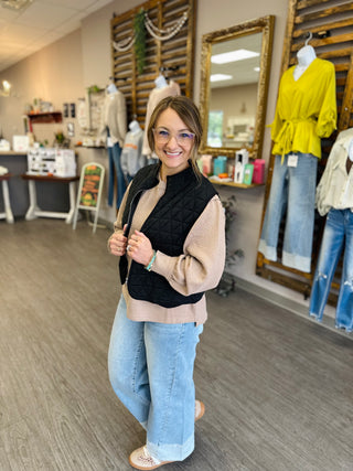 Woman wearing a Timing quilted puffer vest layered over a neutral waffle knit sweater with wide-leg jeans.