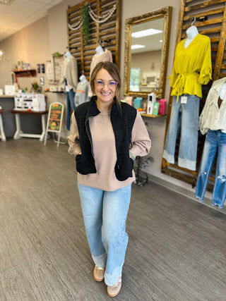 Woman wearing a quilted puffer vest over a neutral sweater and light jeans in a boutique.