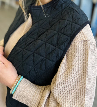 Woman wearing a quilted puffer vest layered over a cable knit sweater with beaded bracelets.