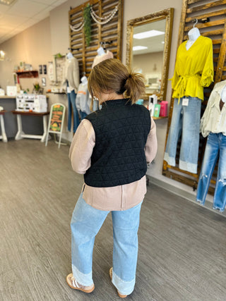 Back view of a woman wearing a quilted puffer vest layered over a waffle knit top with jeans.