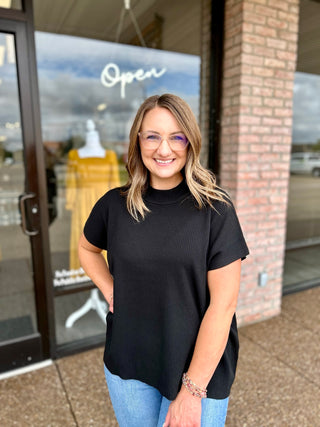 Woman smiling outside boutique wearing a ribbed mock neck short sleeve sweater top with jeans.