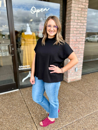 Woman wearing a ribbed mock neck sweater top paired with light wash jeans and wedge sandals.