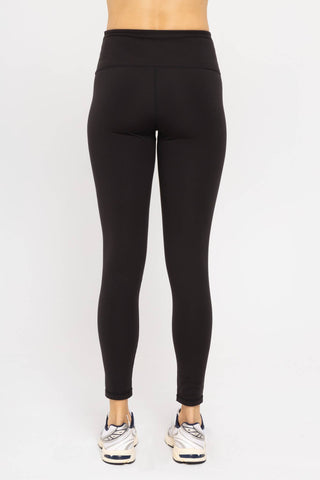 Black high-waisted leggings with tummy control panel shown from behind on model wearing sneakers