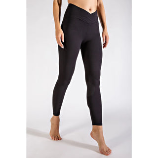 Woman wearing black high-waisted leggings with V-shaped waistband, standing barefoot against white background.