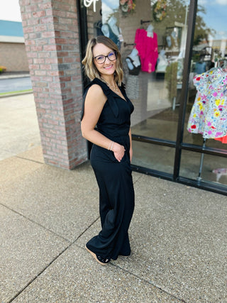 Woman wearing black sleeveless wide leg jumpsuit standing outside boutique storefront